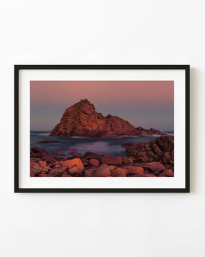 Sugarloaf Rock in Western Australia glows in warm light above a soft blue sea.