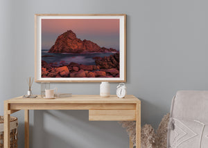 Warm orange light falls across Sugarloaf Rock and foreground coastal stones.