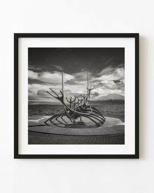 Sun Voyager sculpture on Reykjaviks waterfront beneath dramatic clouds in black and white.