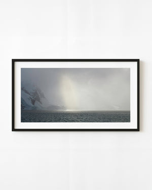 Sunlight glows through an Antarctic snowstorm above dark sea and snowy mountain slopes.