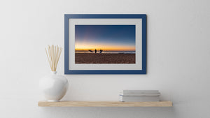 Long Reef Beach at sunrise with dark figures and a broad blue sky.