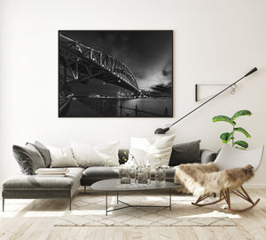 Monochrome harbour view with the Opera House beneath an illuminated bridge.