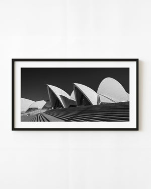 Sydney Opera House roof shells above broad steps in a panoramic black and white photograph.