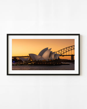 Sydney Opera House and Harbour Bridge beneath a glowing amber sky.