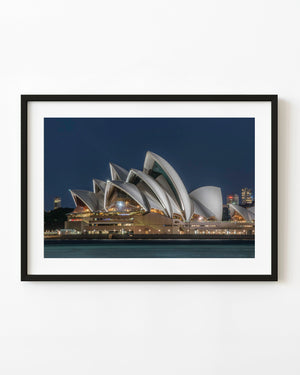 Sydney Opera House illuminated against a deep blue evening sky above harbour water.