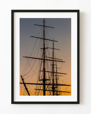 Tall ship masts and intricate rigging silhouetted against a warm sunset sky.