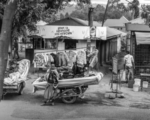 Jackets hang above folded clothes on a wheeled stall along a Tanzanian street.