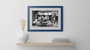 Monochrome street photograph of people, clothing stalls and small roadside shops in Tanzania.