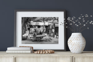 Tanzania market scene with garment displays, shop signs and shaded trees.
