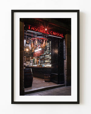 Tasca El Corral in Barcelona with a glowing red sign, hanging cured meats and a warmly lit bar.