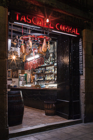 Open Barcelona tavern doorway reveals hanging hams, bottles and dark wooden furnishings.