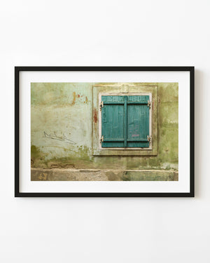 Closed teal wooden shutters on a weathered pale green wall in Romania.