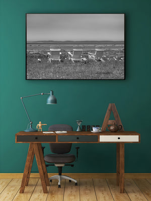 Quiet shoreline scene with three chairs beneath a wide pale sky.