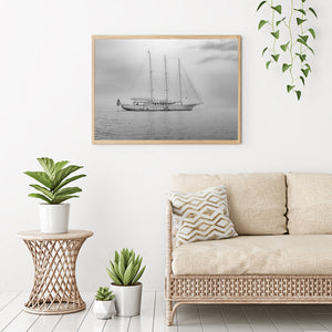 A white yacht with three tall masts lies still on calm water.