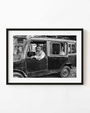 Three men look from the windows of a weathered vehicle in Mysore, photographed in black and white.