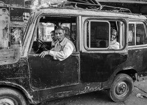 Men seated inside an old Mysore truck with peeling paint and open side windows.