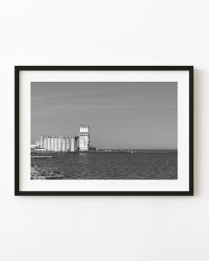 Abandoned Thunder Bay grain elevator beside rippled waterfront water in black and white.