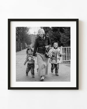 Tibetan mother walks with two children along a Qinghai street in black and white.