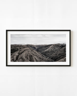 Layered Tibetan mountain ridges and a distant snowy range in a panoramic monochrome photograph.