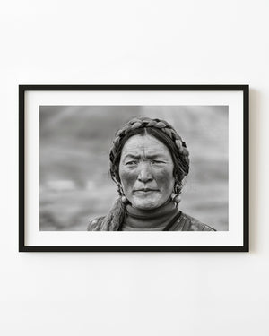 Tibetan woman with braided hair and ornate earrings in a black and white close portrait.