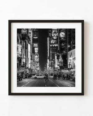 Times Square at night with pedestrians, traffic and illuminated signs in black and white.