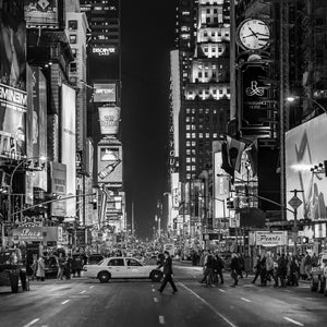 People cross a New York street beneath glowing billboards and tall buildings.