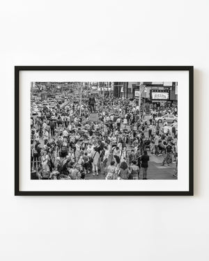 Dense Times Square crowds and traffic around a central statue in black and white.