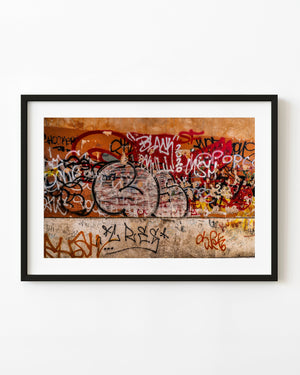 Layered graffiti across a weathered orange wall in Tivoli
