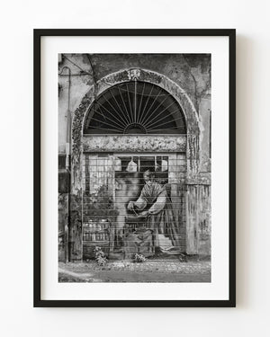Painted shutter beneath a weathered stone arch in Tivoli, black and white
