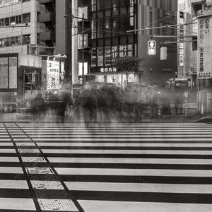 Zwart-witfoto van een stadsstraat met een zebrapad en wazig bewegingseffect.