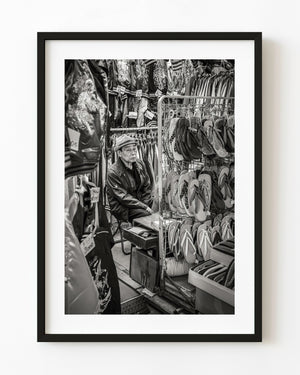 Tokyo market vendor seated among sandals and clothing in black and white