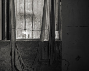 Window light passing through a worn curtain in a dark room