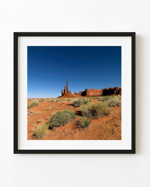 Totem Pole Rock in Monument Valley above red desert sand beneath a blue sky