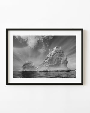 Towering Antarctic iceberg with sculpted cliffs above dark water in black and white.