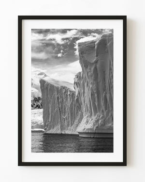 Towering Antarctic ice cliffs above dark water in black and white.