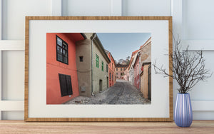 A winding cobbled street between weathered pastel houses in Transylvania.