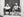 Black and white Trinidad street portrait of two seated men with cigars and a birdcage.