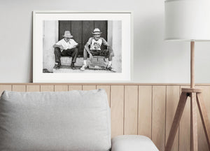 Monochrome street photograph of two men smoking cigars beside a small birdcage.
