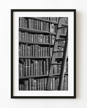 Wooden ladder against shelves of antique books at Trinity College Library in black and white.
