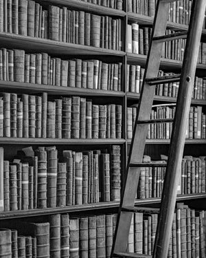 Trinity College library shelves packed with old volumes beside a tall wooden ladder.