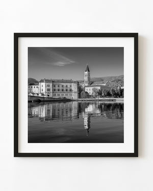 Trogir cathedral tower and historic waterfront reflected in rippling water in black and white.