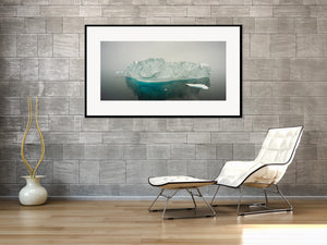 A fractured iceberg with turquoise submerged ice in a quiet polar seascape.