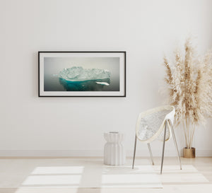 Turquoise ice and dark water surround a snow-covered Antarctic iceberg.