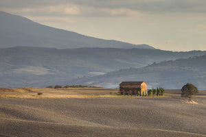 Warm light falls on a lone farmhouse in the rolling Tuscan countryside.