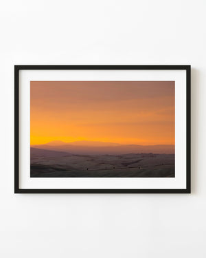 Rolling Tuscan hills beneath a glowing orange sunset sky.