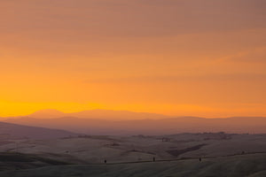 Layered hills and quiet fields in Tuscany under golden-orange evening light.
