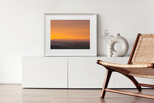 Tuscan countryside with distant mountain silhouettes beneath a luminous sunset.