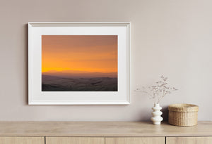 Tuscany landscape with dark rolling farmland and a vivid golden-orange horizon.