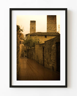 Warm-toned Tuscan stone laneway beneath tall medieval towers.