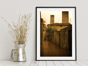 Vertical photograph of historic Tuscan towers above a winding stone passage.